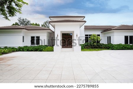 Elegant mansion entrance located in the Pinecrest village, in Miami-Dade, Florida, with large tropical vegetation around it, short grass, driveway, summer weather, trees, palm trees, blue sky