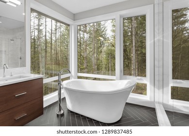 Elegant Master Bathroom Interior In New Luxury Home, Featuring Bathtub, Sink, Tile Floor, And Beautiful View Of Trees And Forest. 