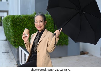 Elegant Mature Business Woman Holding Takeaway Coffee Sitting Under Umbrella At City Street