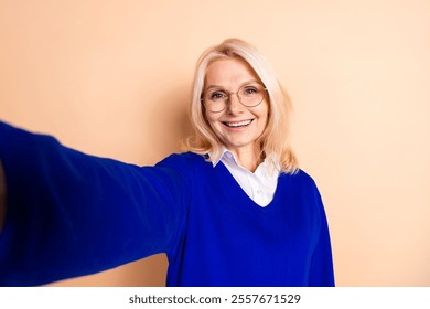 Elegant mature woman smiling in blue jumper against beige background, capturing professional and confident essence in casual attire. - Powered by Shutterstock