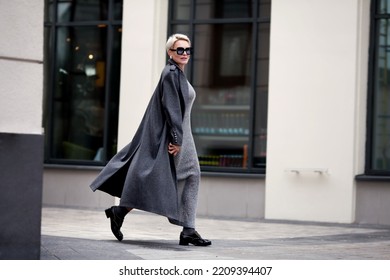Elegant Mature woman walks city street , wears stylish clothes, gray wool coat, long dress, black shoes and glasses. Trending outfit
