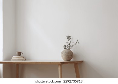 Elegant Mediterranean home design. Textured vase with olive tree branches, cup of coffee. Books on wooden table. Living room still life. Empty wall copy space. Modern interior, no people. Home office. - Shutterstock ID 2292735913