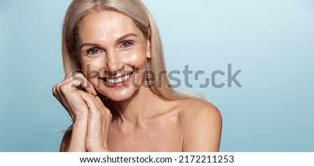Elegant middle aged woman, head and shoulders with glowing skin, nourished, moisturized face and body, smiling at camera, blue background