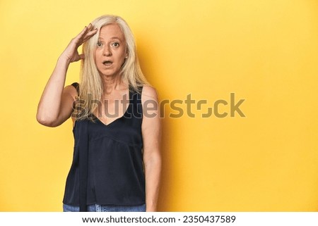 Elegant middle-aged woman in black top, yellow studio shouts loud, keeps eyes opened and hands tense.