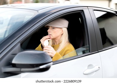Elegant middle-aged woman eating chewing gum in a car behind the wheel