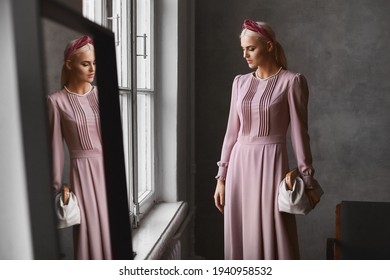 An Elegant Model Woman With Perfect Makeup Wearing A Pink Evening Dress, Keeping Purse, And Posing In Vintage Interior Near The Mirror