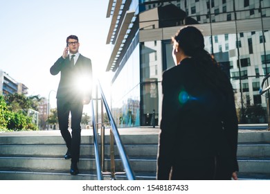 Elegant Modern Businessman Speaking On Mobile Phone And Woman In Suit Walking Against Each Other On Street Stairs In Back Lit