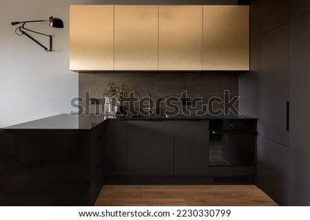 Elegant and modern kitchen interior with golden upper cupboards and black drawers, countertop, sink, tap and furniture