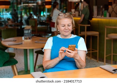 elegant modern older mature senior woman with glasses is sitting in a cafe with a mobile phone with a cup of tea. The retirement age is 60 years.