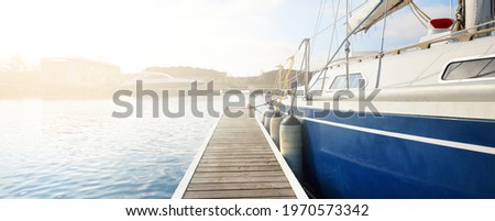 Elegant and modern sailing boats (for rent) moored to a pier in a yacht marina on a clear day. Sweden. Blue sloop rigged yacht close-up. Vacations, sport, amateur recreational sailing, cruise