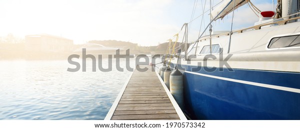 Elegant and modern sailing boats (for rent) moored\
to a pier in a yacht marina on a clear day. Sweden. Blue sloop\
rigged yacht close-up. Vacations, sport, amateur recreational\
sailing, cruise