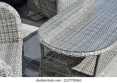 Elegant Modern Woven Garden Furniture (chairs And A Low Glass Top Table) On A Grey State Stone Patio. Close Up Monochrome Design Detail. Outdoors On A Bright Sunny Day With Textured Shadows