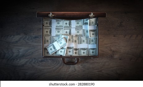 Elegant open briefcase filled with dollar packs on a wooden desktop in the dark, top view
