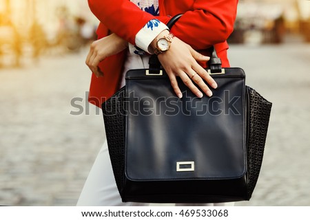 Elegant outfit. Close up of black leather bag handbag in hands of stylish business woman. Fashionable girl on the street. Sunny day. Female fashion concept.  City lifestyle