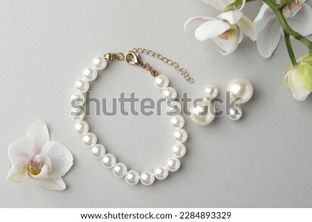 Elegant pearl earrings, bracelet and orchid flowers on white background, flat lay