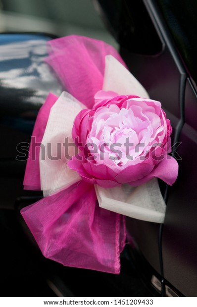 Elegant pink and red satin rose of fabric and\
ribbons decorate the wedding car. Close up with selective focus and\
neutral soft\
background.