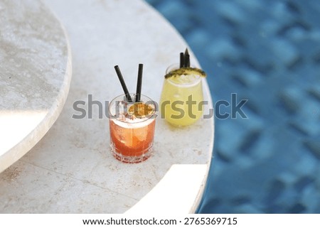 Elegant poolside summer scene featuring two colorful cocktails in green and red tones placed beside a swimming pool creating a luxury resort lifestyle composition the image highlights refreshing summer drinks served in stylish glassware against a clear blue water background natural sunlight enhances reflections vibrant colors and clean modern aesthetics the scene represents high end hospitality beach club atmosphere vacation relaxation and social leisure ideal for concepts such as summer holiday pool party luxury travel resort branding cocktail menu beverage advertising hospitality industry and commercial stock photography usage