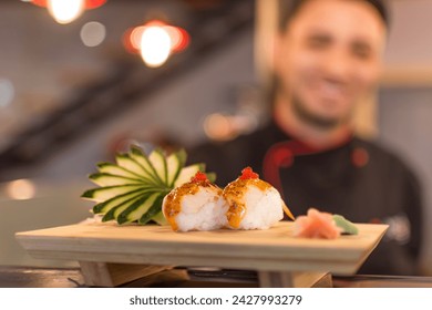 An elegant presentation of salmon nigiri in close-up on a cutting board, with the smiling sushi chef blurred in the background - Powered by Shutterstock