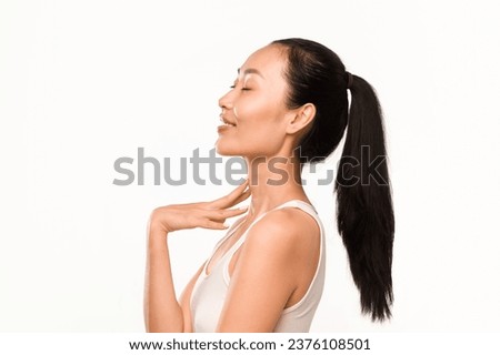 Elegant profile of Asian woman with sleek long black hair tied in a ponytail, posing with eyes closed, showcasing serene expression, touches her neck with grace, white background