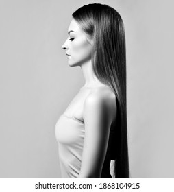 Elegant profile of young beautiful woman with silky long straight hair standing and looking down over grey background. Hairstyle, hairsalon, hairdresser, fashion concept