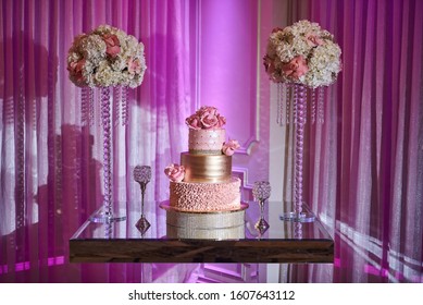 Elegant Quinceanera Cake On A Glass Table Surrounded By Big Flower Arrangements.