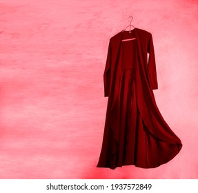 Elegant red long dress on metal clothes rack isolated over pink wall background.
