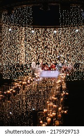 An Elegant Road To The Wedding Altar At An Outdoor Ceremony Late In The Evening. Garlands Hanging From Above Are Reflected In The Mirrored Floor, Candles In Glass Cases Are Burning On The Sides.