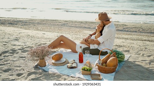 Elegant romantic couple having picnic at the beach, embracing and lying blanket. Romance, dating and love concep
