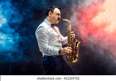 Elegant saxophonist plays jazz on dark background in a smoke - Shutterstock ID 412319752