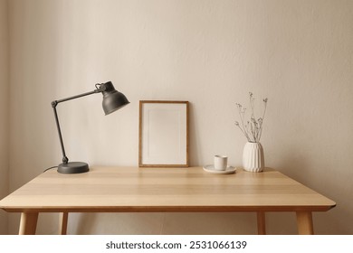 Elegant Scandinavian interior, living room. Blank wooden picture frame mockup on table. Modern grey lamp, dry flowers, white vase. Cup of coffee, tea. Working space, home office, beige wall background