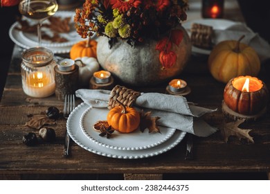 Elegant seasonal fall table setting with floral composition in a pumpkin vase as a centrepiece. White wine, burning candles, romantic cozy atmosphere of family dinner, private autumn wedding - Powered by Shutterstock