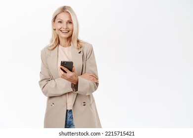 Elegant Senior Blond Woman, 50 Years Old, Using Mobile Phone, Looking Happy And Smiling At Camera, Standing Over White Background