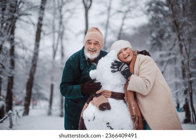 Elegant senior couple building snowman during cold winter snowy day. - Powered by Shutterstock