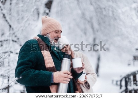 Elegant senior couple having hot tea outdoor, during cold winter snowy day.