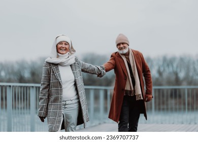 Elegant senior couple walking near the river, during cold winter day. - Powered by Shutterstock