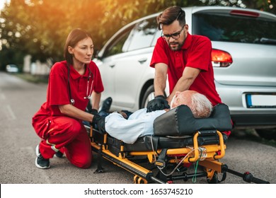 Elegant senior man with heart attack symptoms sitting on the road emergency medical service workers trying to help him. Driver assistance service.  - Powered by Shutterstock