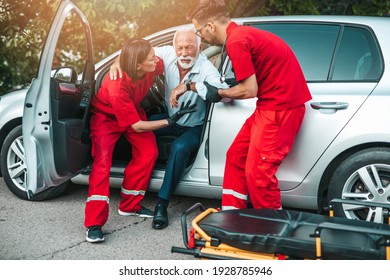 Elegant Senior Man With Heart Attack Symptoms Sitting In The Car, Emergency Medical Service Workers Trying To Help Him. Driver Assistance Service. 