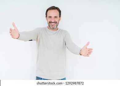Elegant senior man over isolated background looking at the camera smiling with open arms for hug. Cheerful expression embracing happiness.
