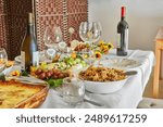 An elegant Shavuot holiday table with wine, cheese, fruit and holiday decorations, ready for a traditional Jewish holiday meal. Happy Shavuot inscriptions in Hebrew.