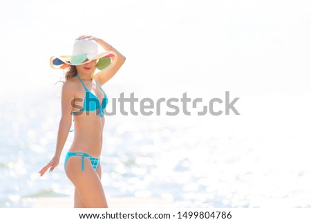 Elegant slim girl by the sea. Beautiful young slim woman with a beautiful figure in a hat is standing on the sea beach.