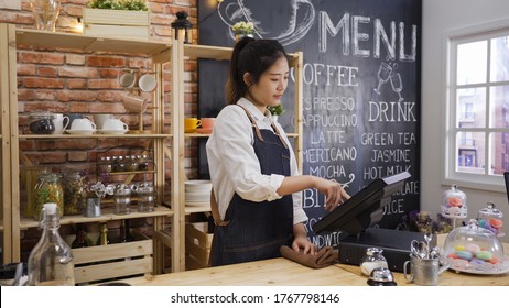 elegant smiling japanese shop assistant woman using pos point of sale terminal to put in order from notepad at restaurant register. charming girl worker waitress using tablet on bar counter in cafe - Powered by Shutterstock