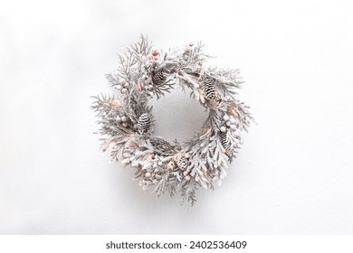 Elegant snow-covered Christmas wreath with small lights hanging on a white wall - Powered by Shutterstock