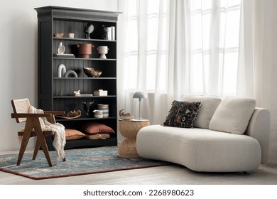 Elegant sofa in eclectic style living room with classic bookcase, rattan chair and coffee table and decorative carpet