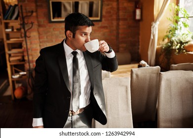 Elegant South Asian Indian Business Man In Black Suit Posed Indoor Cafe And Drinking Tea.