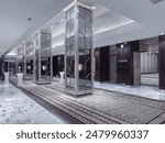 An elegant and spacious hotel lobby with a modern design. The lobby features a combination of marble flooring and patterned carpeting, complemented by dark wood paneling and decorative mirrors.