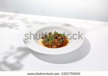 Elegant stew beef with mashed potatoes in  restaurant. Beef bourguignon on light background with shadows of leaves. Braised black angus meat with potato cream in summer menu