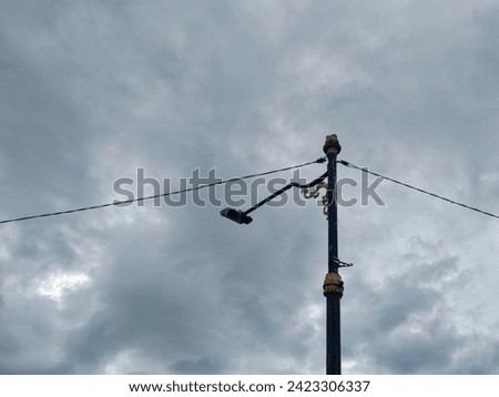 An elegant street lamp post stands against a dramatic cloudy sky. The lamp post, adorned with intricate golden details, contrasts with the impending gloom of the overcast weather.