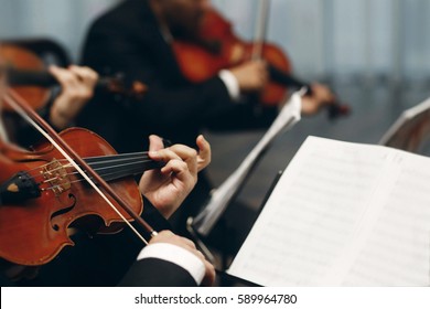 Elegant string quartet performing at wedding reception in restaurant, handsome man in suits playing violin and cello at theatre play orchestra close-up, music concept