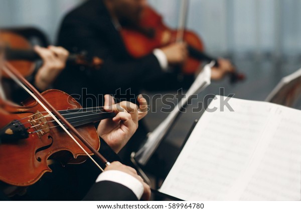 Elegant string quartet
performing at wedding reception in restaurant, handsome man in
suits playing violin and cello at theatre play orchestra close-up,
music concept
