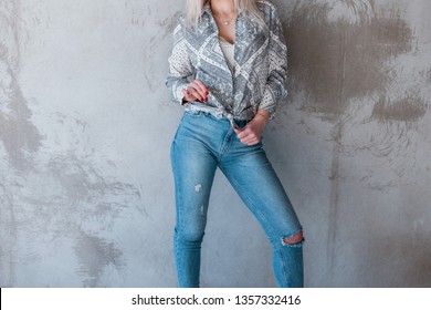 Elegant stylish young woman blonde in a stylish white T-shirt in vintage ripped jeans in a fashionable shirt jacket with a vintage pattern near the gray wall. Modern fashion women's clothing.